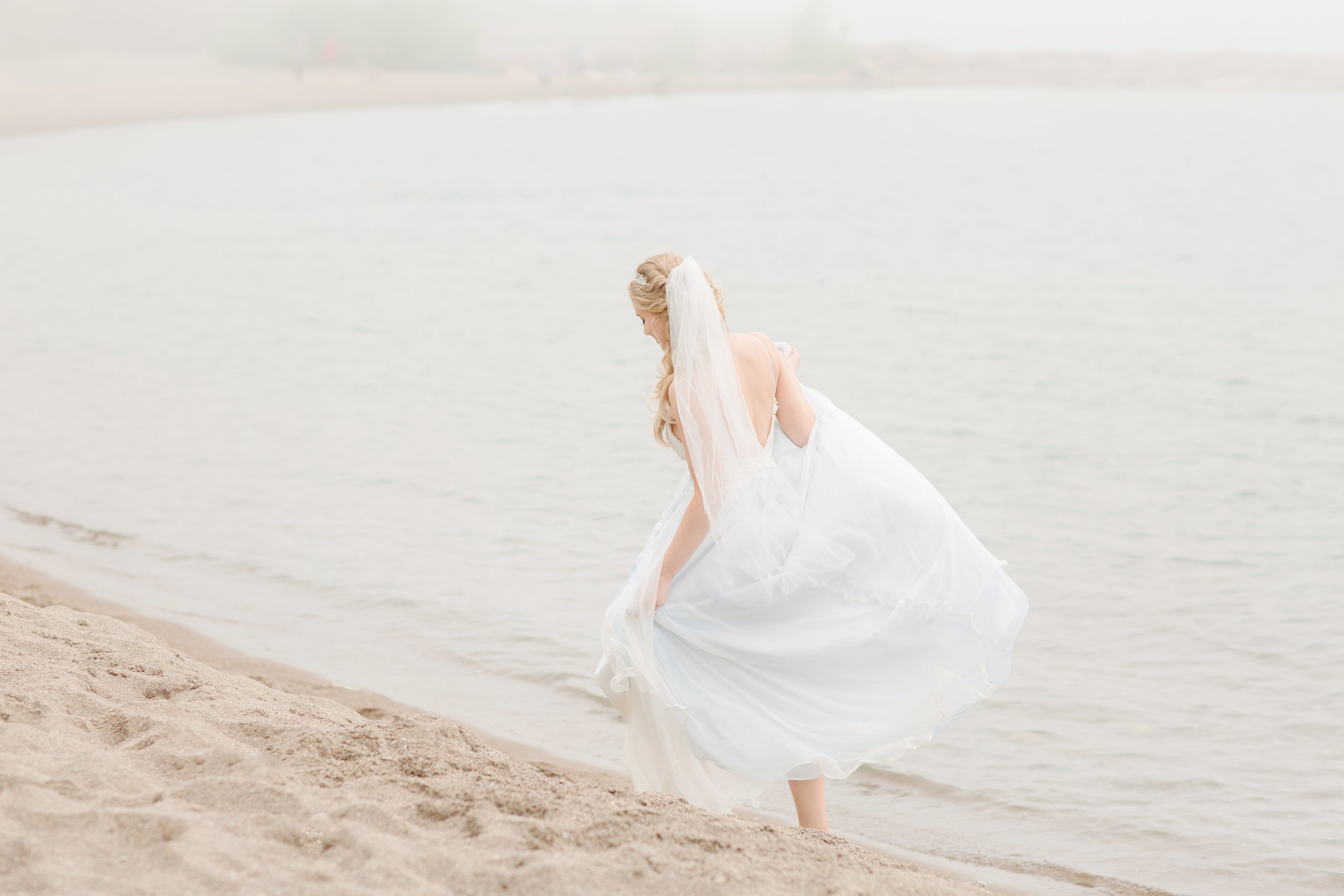 Bride frolicking happily along the beach in white strapless wedding gown with veil - Orange Blossom Bridal.